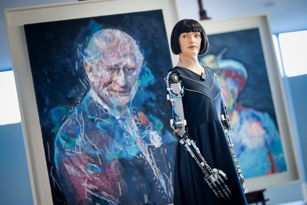Ai-Da, a humanoid AI artist robot, stands in front of its paintings of UK royalty